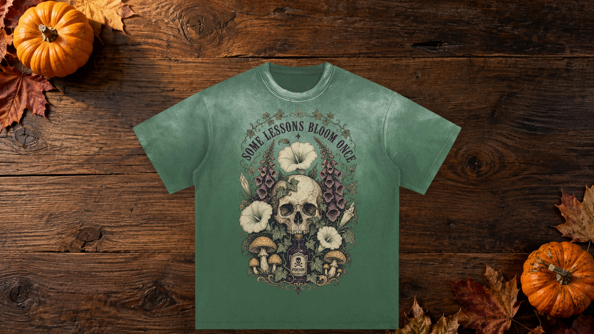 Green Some Lessons Bloom Once graphic tee on a wooden fall table with pumpkins and autumn leaves.