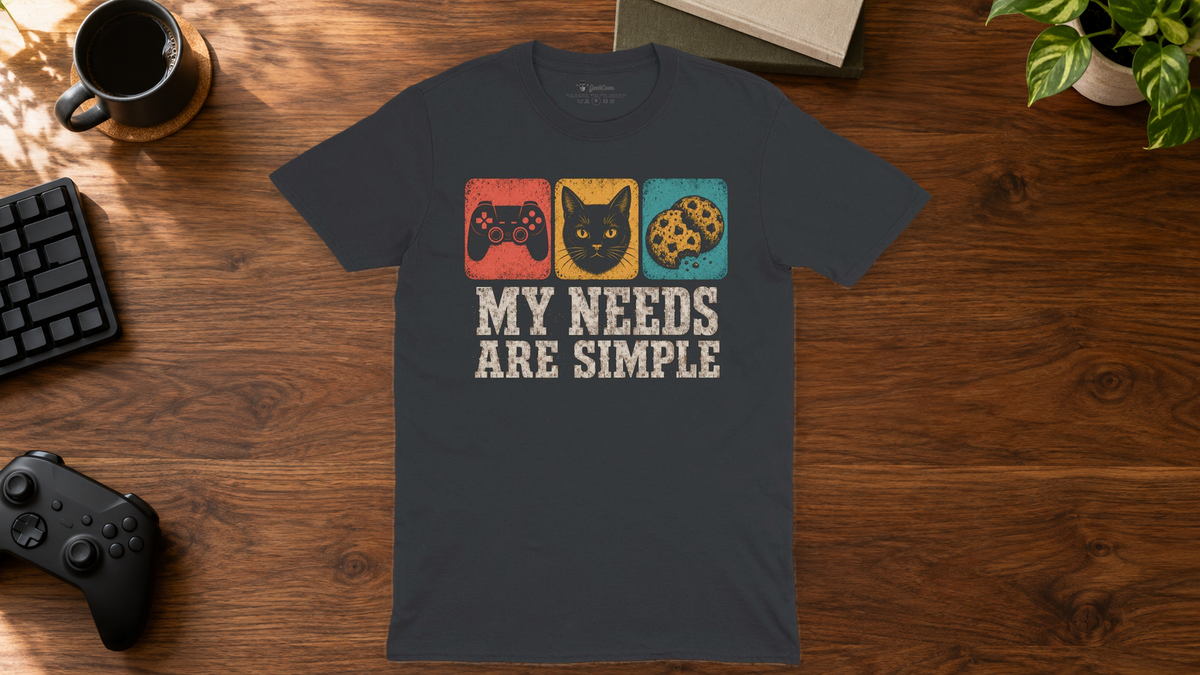Black My Needs Are Simple graphic tee laid flat on a gaming desk with a controller, keyboard, coffee mug, books, and plant.