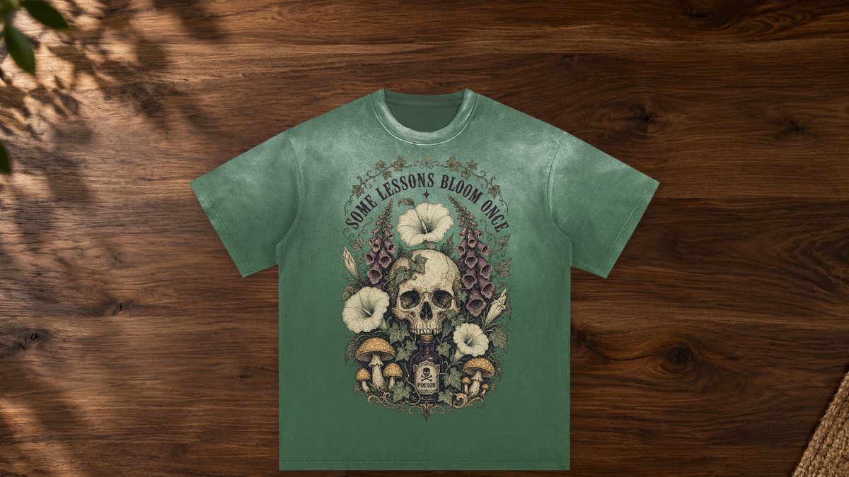 Green Some Lessons Bloom Once graphic tee laid on a warm walnut table.