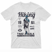 The image depicts a dark t-shirt with a design centered around the theme of hiking. It features the silhouette of a hiker in blue, viewed from the back, wearing a hat and a backpack. Large text above and below the figure reads "Hiking" and "Take a Walk on the Wild Side"