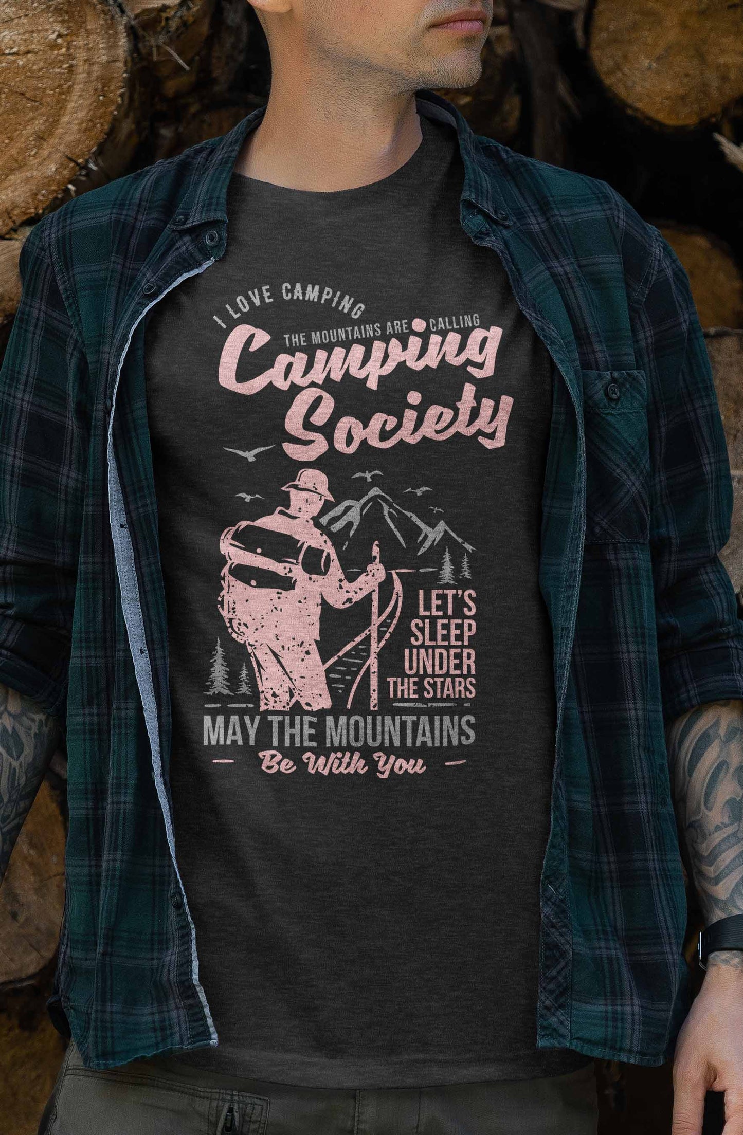 this t-shirt design depicts a hiker in silhouette, facing a mountain landscape. above and below the hiker are phrases like "i love camping, the mountains are calling," and "let's sleep under the stars, may the mountains be with you," all in stylized pink and white fonts on a dark background.