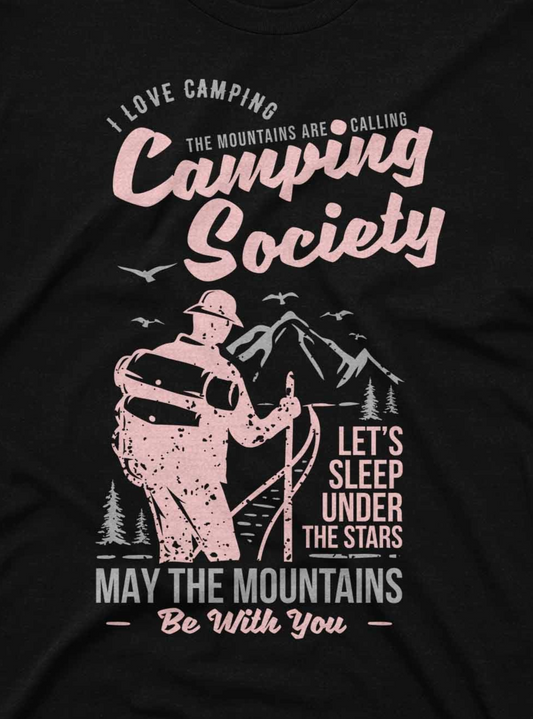 A dark-colored t-shirt displays a camping-themed design with a hiker looking towards a mountain range. Key phrases such as "Camping Society" and "Let's Sleep Under the Stars" frame the image in large, appealing typography, encouraging a connection with nature and outdoor adventures.