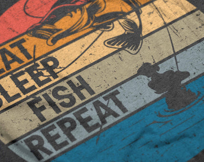 The graphic on the t-shirt presents a vibrant depiction of fishing life in a circular format, with sections colored in sunset hues. "Eat Sleep Fish Repeat" is prominently displayed with dynamic fishing imagery, including a jumping fish and a serene fishing scene, capturing the constant cycle of a passionate angler.