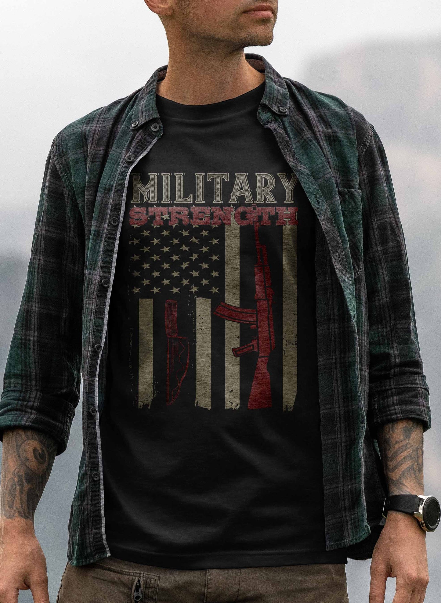 the graphic on the t-shirt presents a rustic american flag in the background with a red silhouette of a rifle and a combat knife. above these images, the phrase "military strength" is printed in a bold, distressed font, conveying a theme of resilience and patriotism.