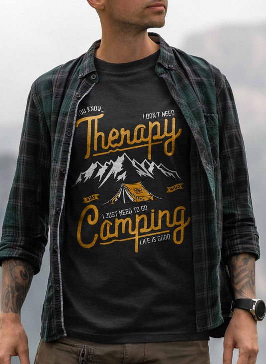 The image features a black t-shirt with a graphic that reads "Therapy - I don't need Therapy, I just need to go Camping - Life is Good". The design includes stylized mountains in the background with a tent in the foreground, all in white and yellow on a black background.