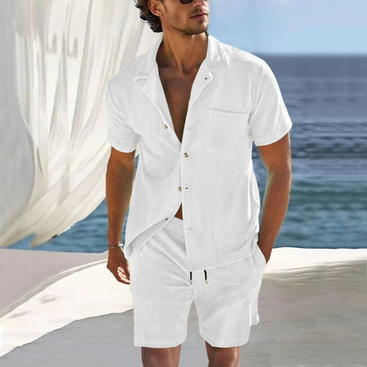 Men's fashion set featuring a white linen short-sleeve shirt and matching shorts, worn by a model against a seaside backdrop.