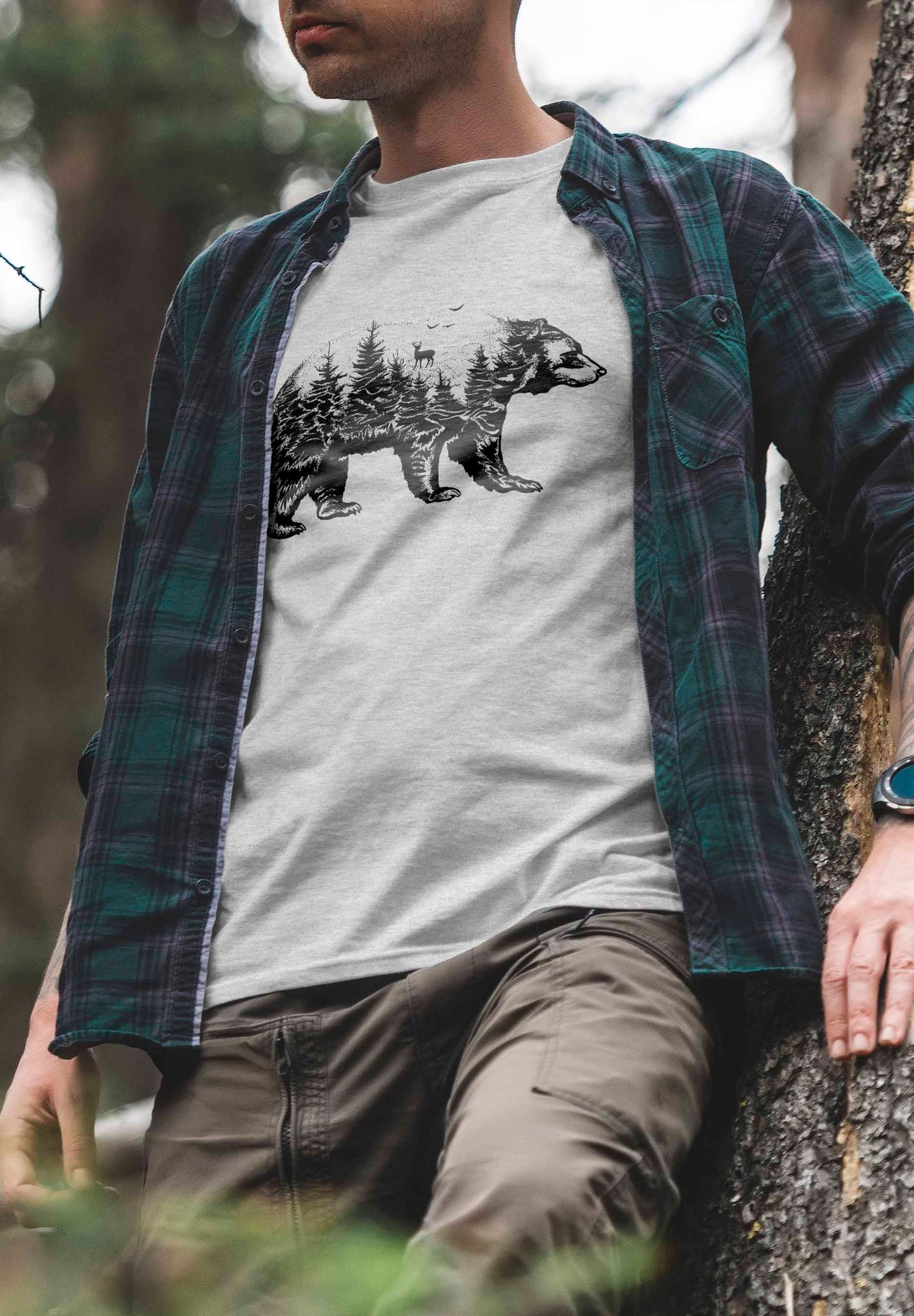 a t-shirt design showing a bear outline that encapsulates a forest environment within its form. the scene includes several trees and a deer, artistically rendered in black and white, evoking a sense of wilderness and natural beauty.