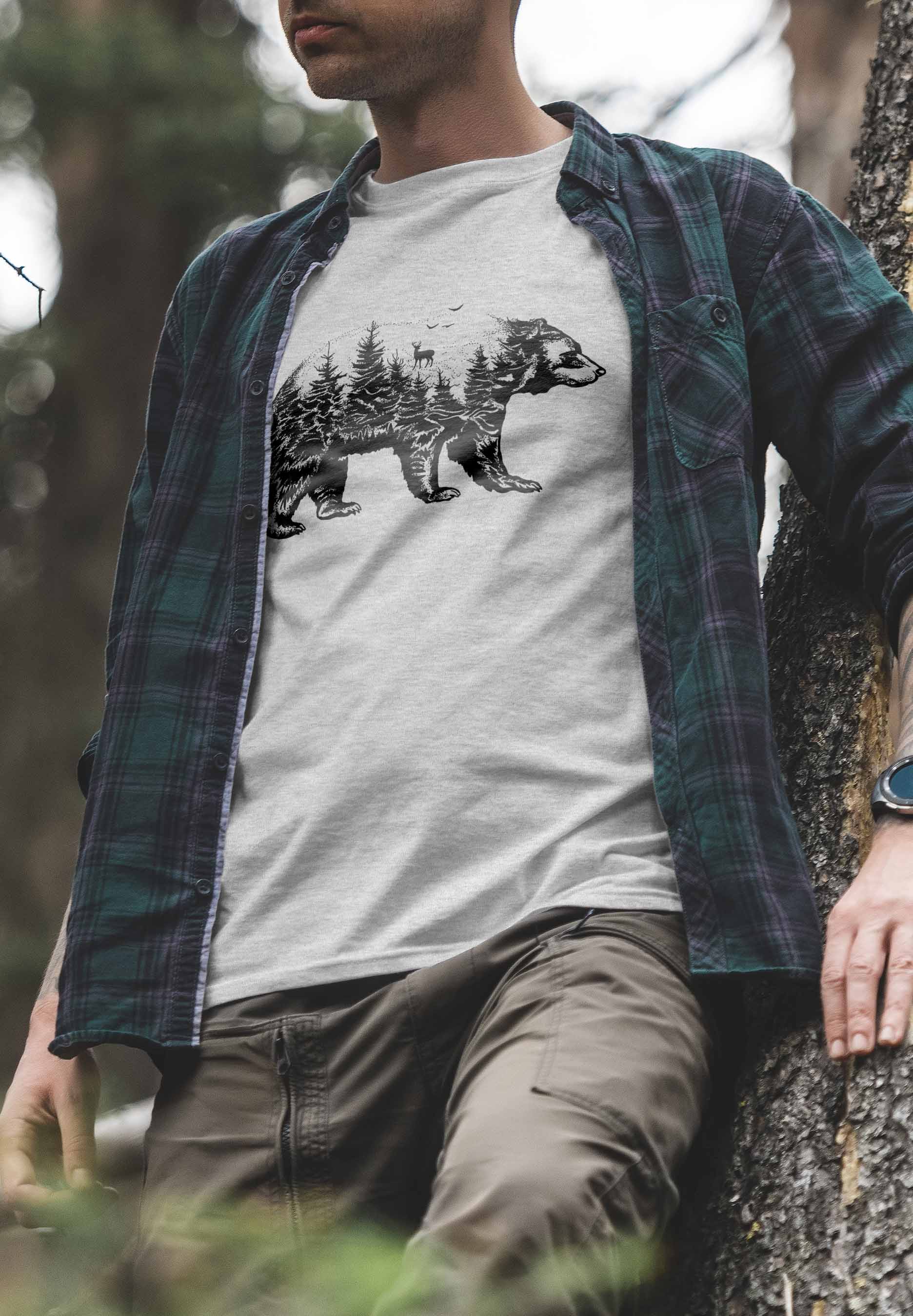 A t-shirt design showing a bear outline that encapsulates a forest environment within its form. The scene includes several trees and a deer, artistically rendered in black and white, evoking a sense of wilderness and natural beauty.