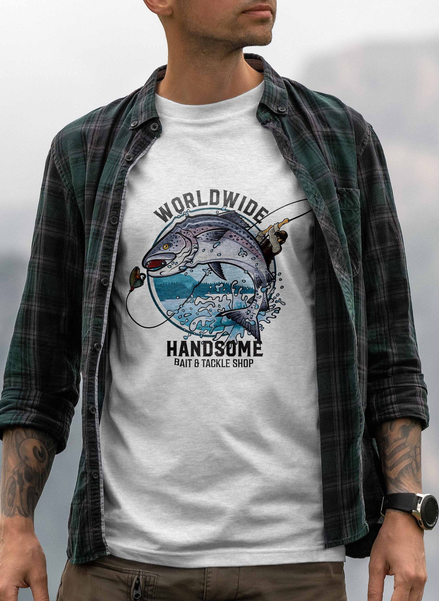 the graphic on the t-shirt presents a visually striking fishing scene, where a fisherman battles a large fish that is leaping out of the water. above and below the scene, the words "worldwide handsome bait & tackle shop" frame the image, conveying a sense of adventure and excitement associated with fishing.